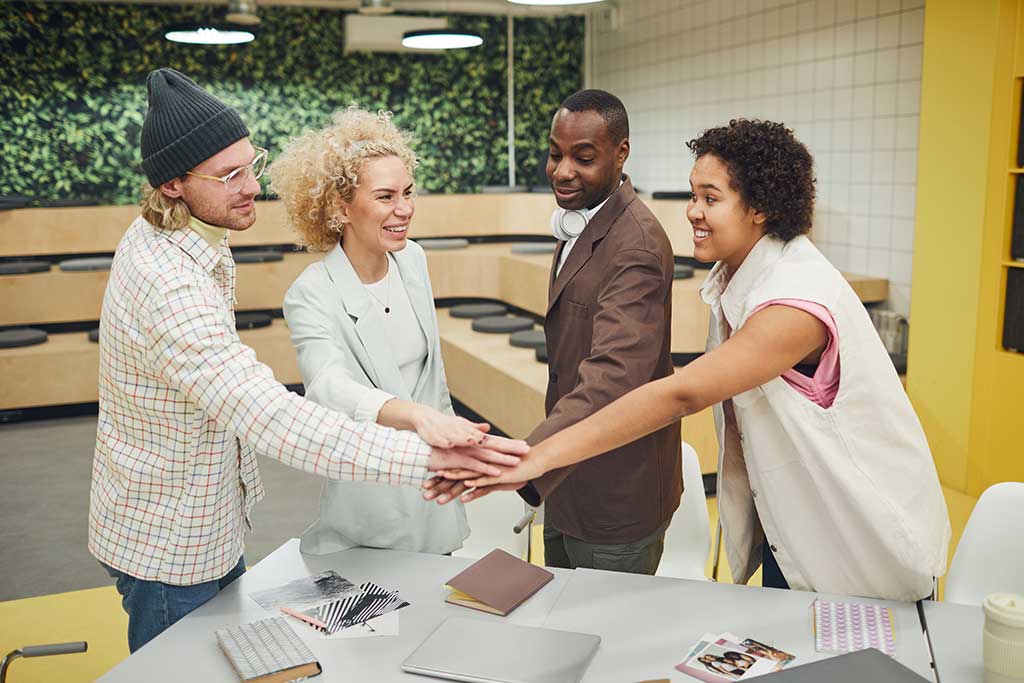 Gemischtes Team aus Männern und Frauen legt im Büro die Hände zusammen als Symbol für Zusammenarbeit.