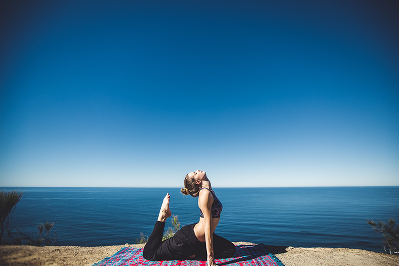 Frau macht Yoga auf Matte am Meer.